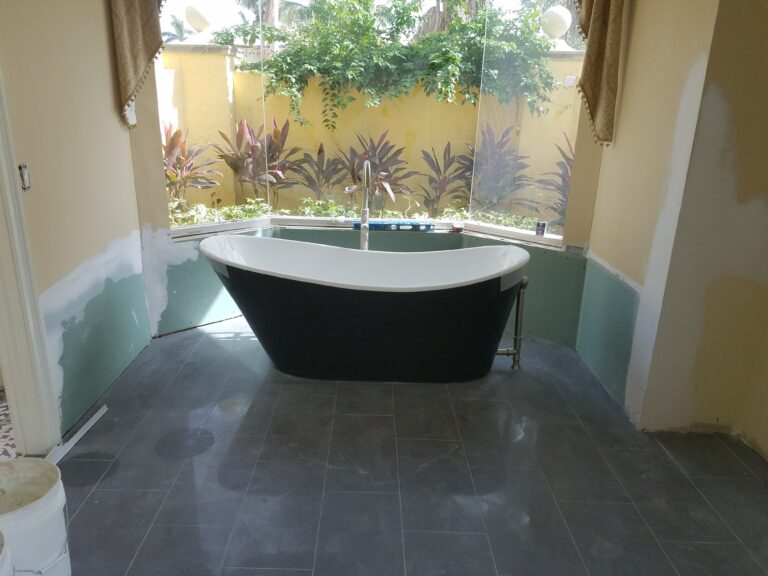 Modern bathroom with a black and white freestanding bathtub facing a large window with tropical garden view, luxury home in Naples, Florida. Dark porcelain tile floor and decorative black and white mosaic wall.